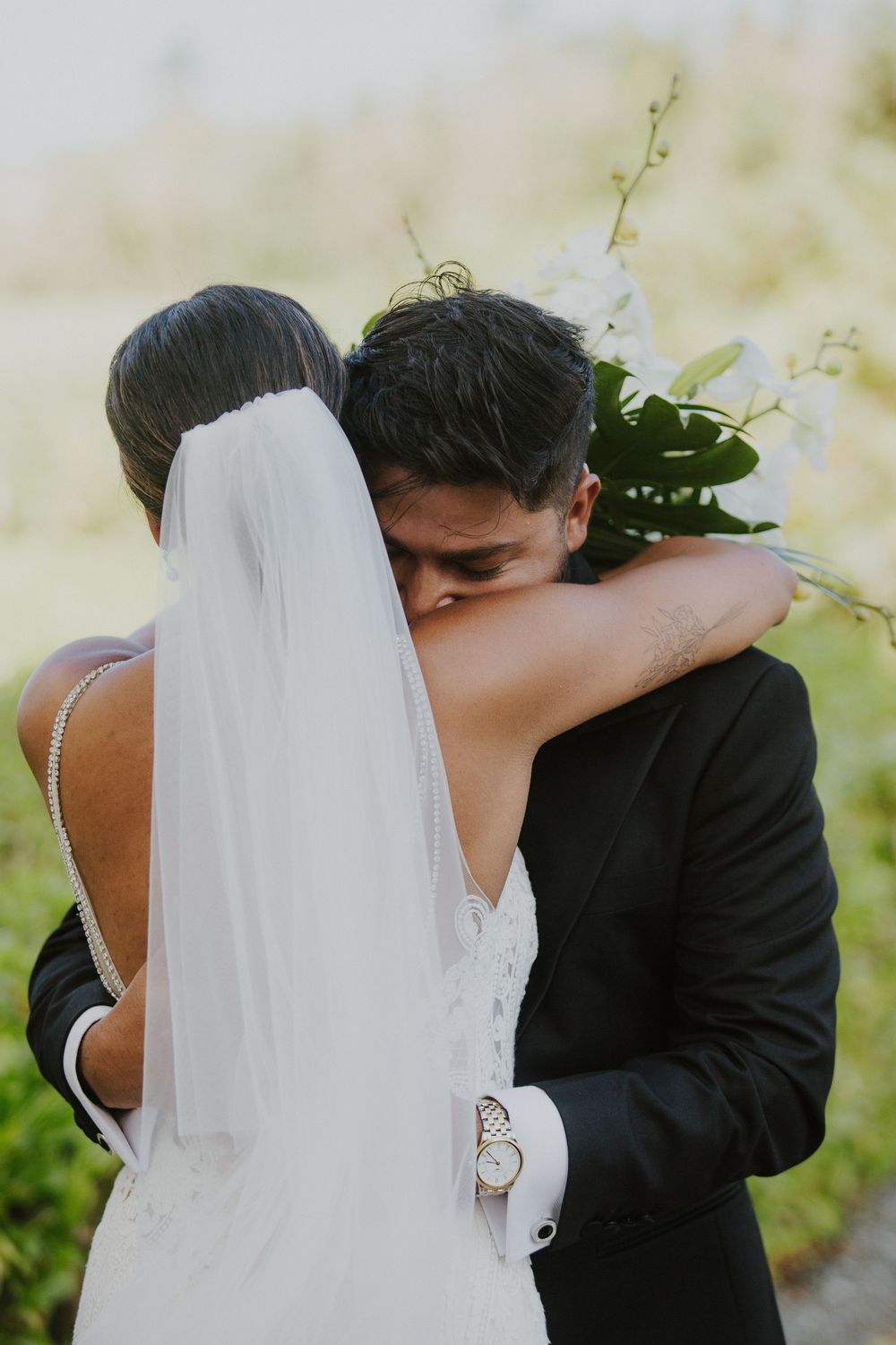 Intimate embrace between newlyweds with flowing veil and tropical greenery.
