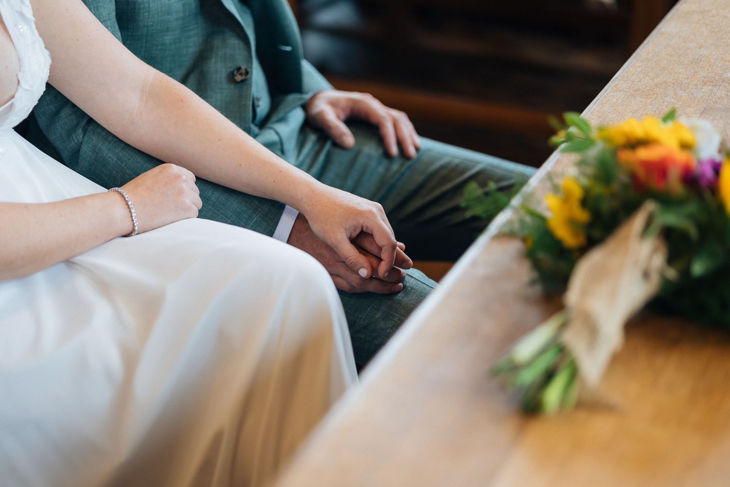 Wedding rings and floral arrangements on wooden table during ceremony preparation.