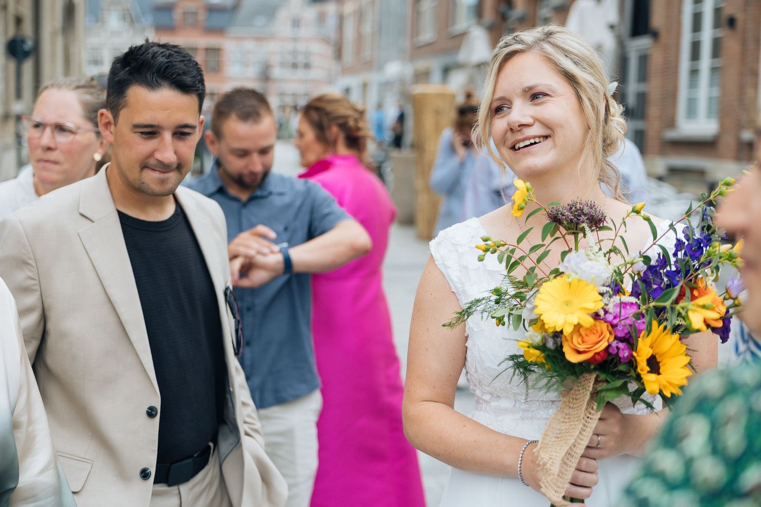 Wedding celebration group in front of historic building with bright sunflower bouquet.