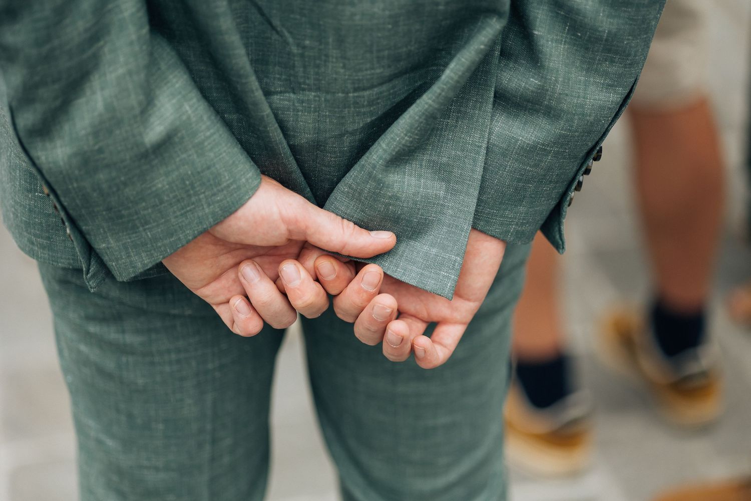 Close-up detail of sage green suit pants and hands during formal occasion.