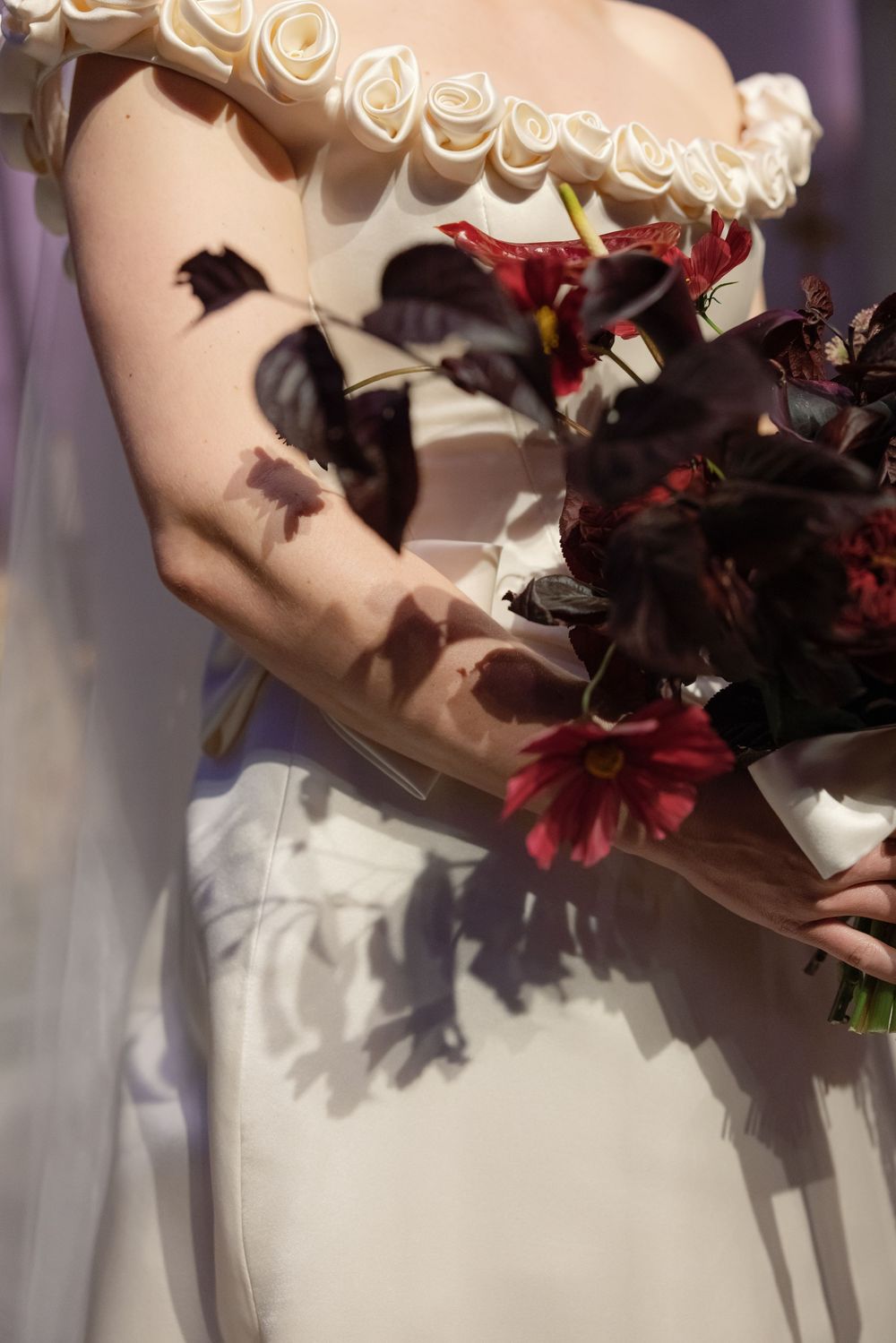 Close-up of a white wedding dress bodice with ruffle detail and dark red floral bouquet.