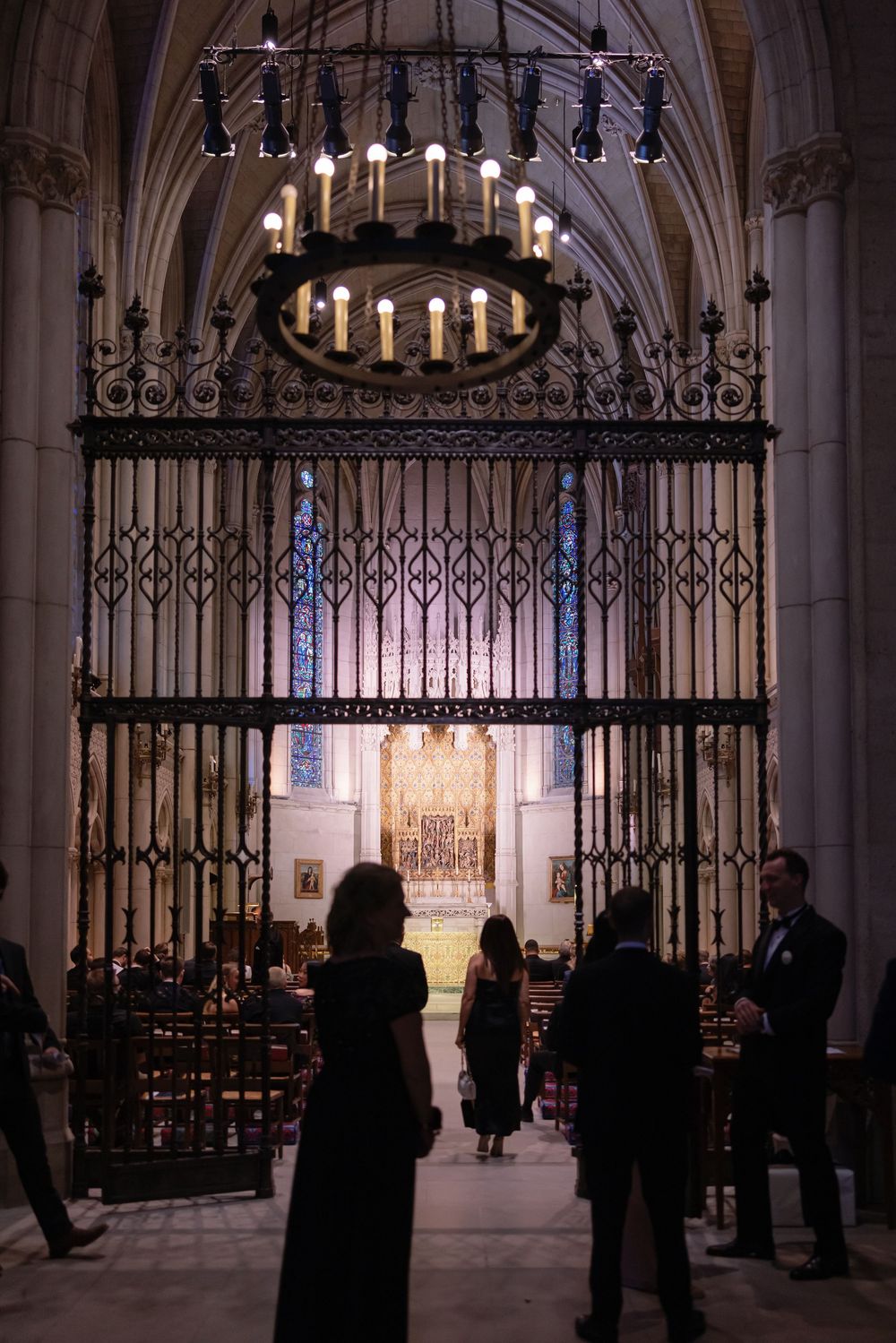 Dark silhouettes against the illuminated interior of a church with iron gates and pews.