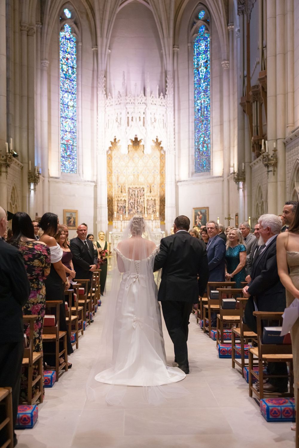 An elegant church wedding ceremony with stained glass windows and guests seated in wooden pews.