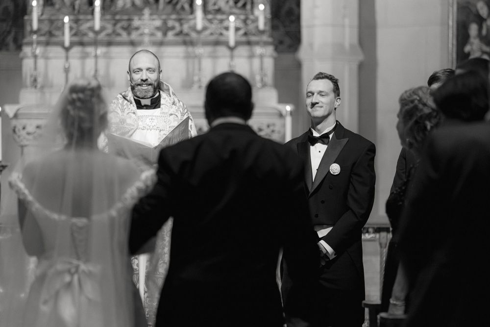 Black and white photo of a wedding ceremony in progress at a church altar with clergy, couple and guests.