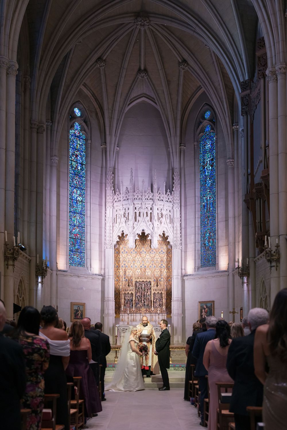 Elegant church interior with stained glass windows and ornate altar during a wedding ceremony.