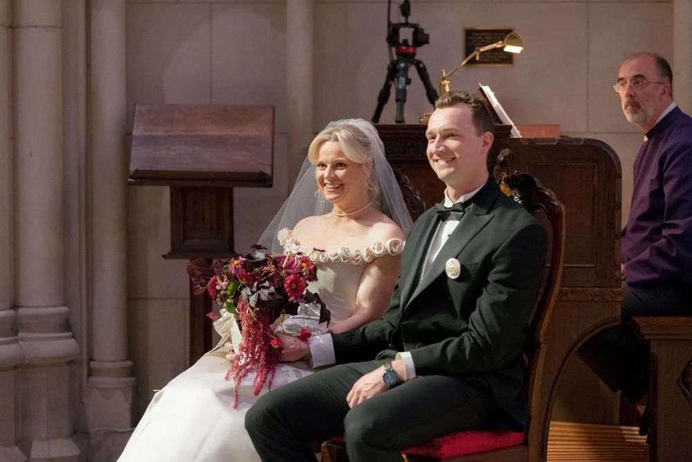 Wedding couple sharing candid moments while seated in church pews.