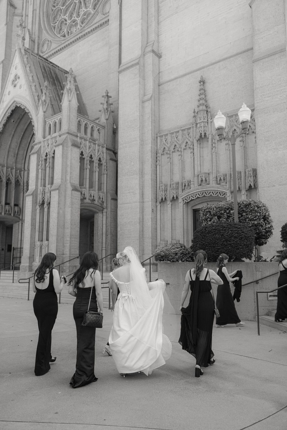 Wedding party in black and white formal attire walking outside a church cathedral.