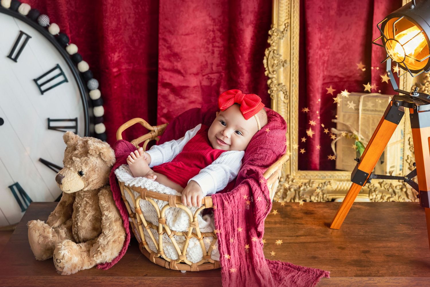 escenario color rojo y dorado bebe de 4 meses posa dentro de una canasta tiene un peluche oso a la de de ella