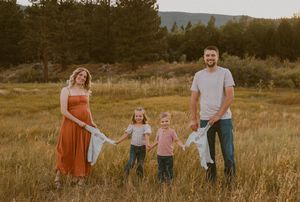 Family wearing coordinated outfits walks together through a golden sunlit field at sunset holding hands.