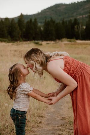 A tender moment shared between two people in a rust-colored dress and plaid top against a mountain backdrop.