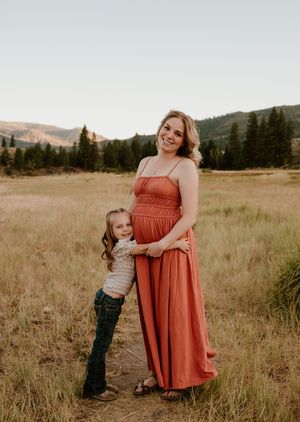 A tender moment captured in a grassy meadow with mountains and evergreen trees in the background at sunset.