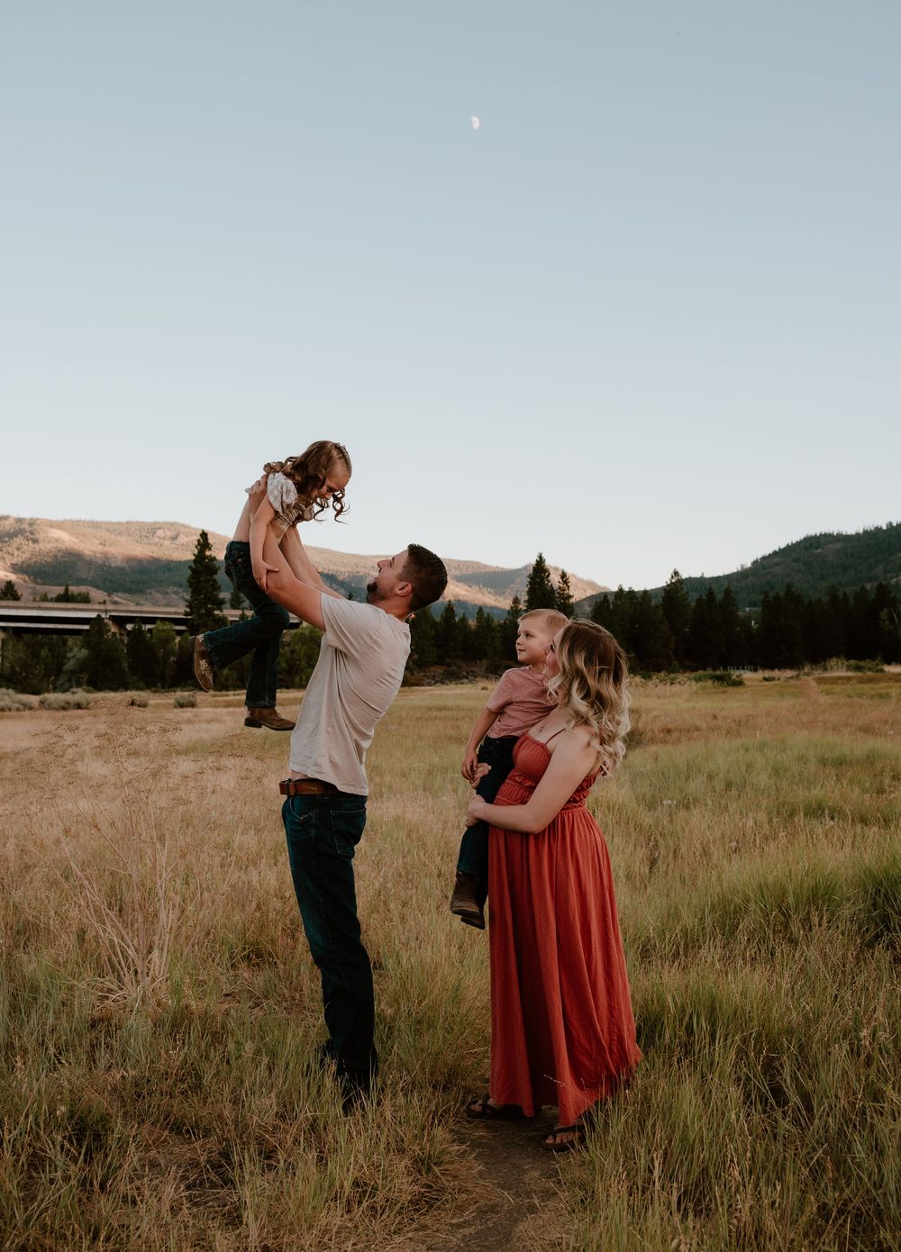 Family enjoying sunset together in grassy field with mountains in background.