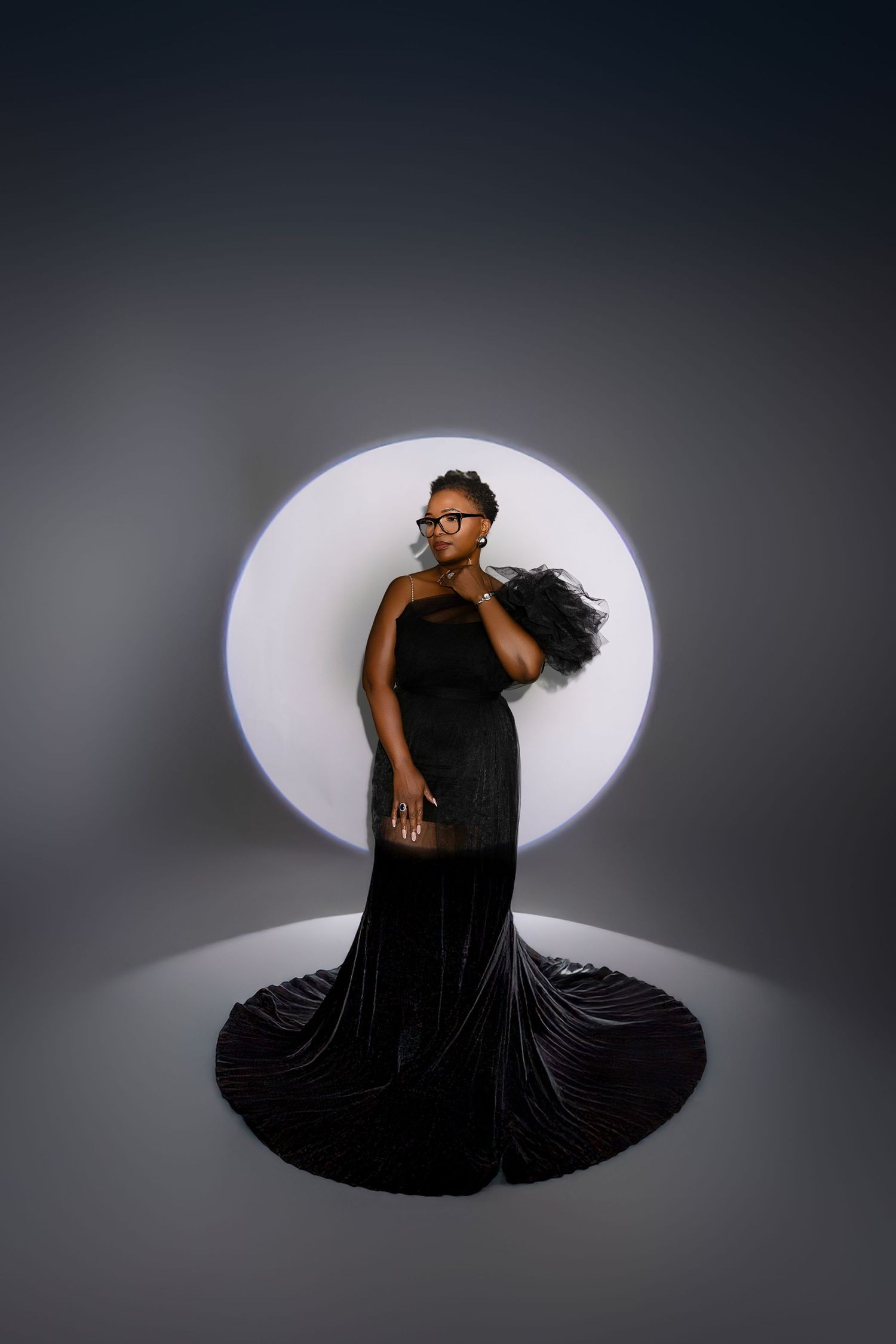 Artistic silhouette of a figure in black attire striking dramatic poses against a circular white spotlight on a gray background.