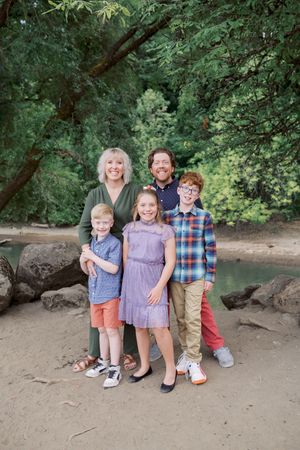 A group of five people stand together on a dirt path surrounded by lush green forest and rocks.