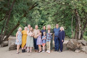 A group of people stand together outdoors on a dirt path surrounded by green trees and large boulders.
