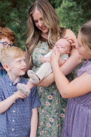 A family of four dressed in blue and purple outfits share loving moments together in a wooded outdoor setting.