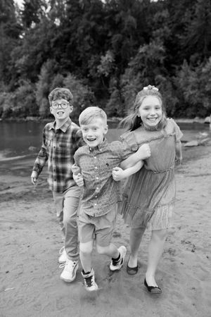 Three children playing and laughing together on a beach with trees in the background.