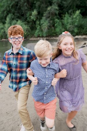 Three young children pose playfully together outdoors wearing coordinated casual outfits at a beach setting.