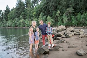 A family enjoys leisure time together along a rocky riverbank surrounded by evergreen trees.