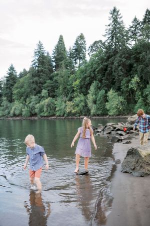 People wading along the shoreline of a river surrounded by tall evergreen trees and rocky banks in the Pacific Northwest.