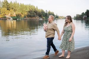 A couple shares tender moments during a waterfront photoshoot along a scenic lake with evergreen trees in the background.