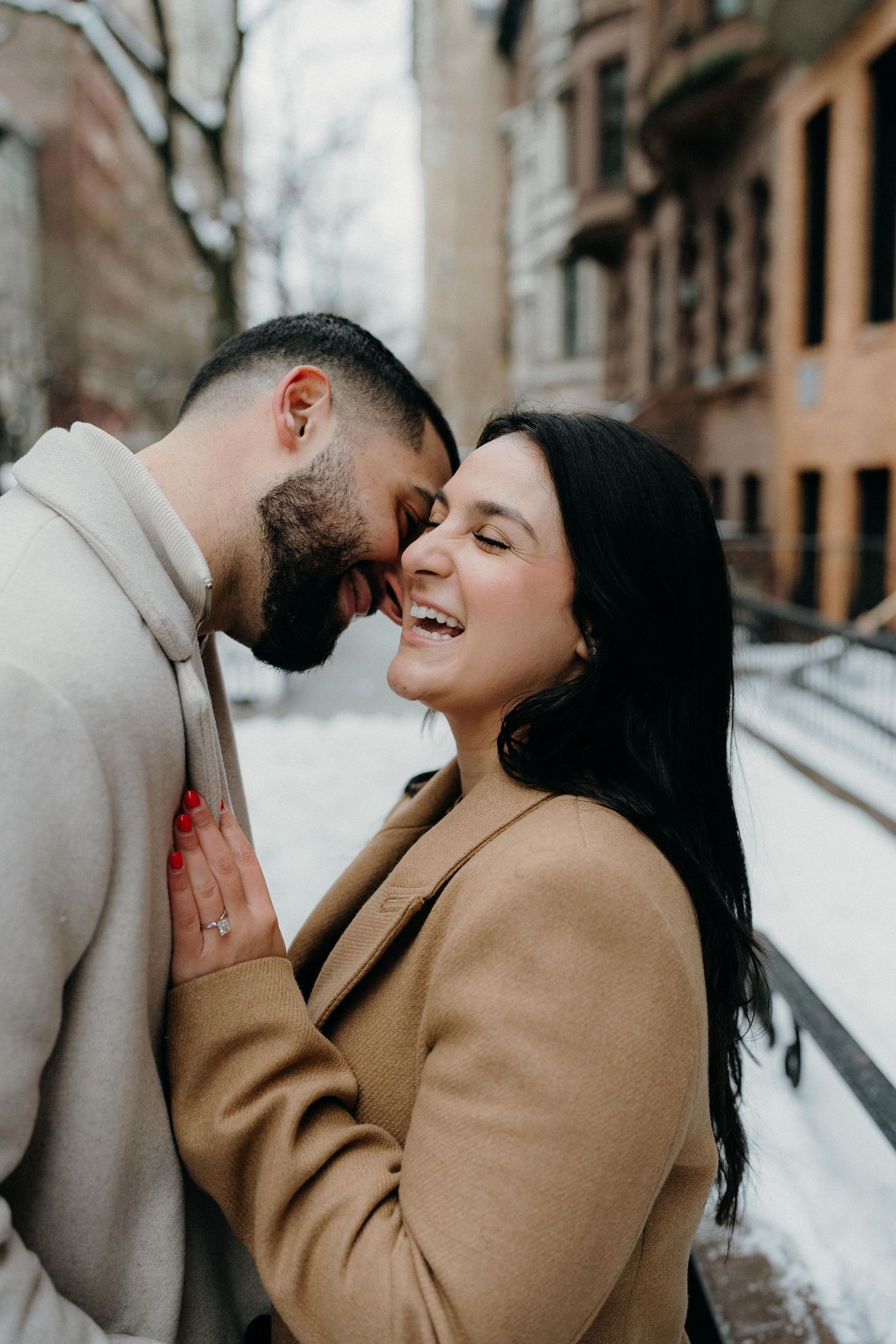 A joyful couple sharing an intimate moment while wearing winter coats on a snowy new york city street.