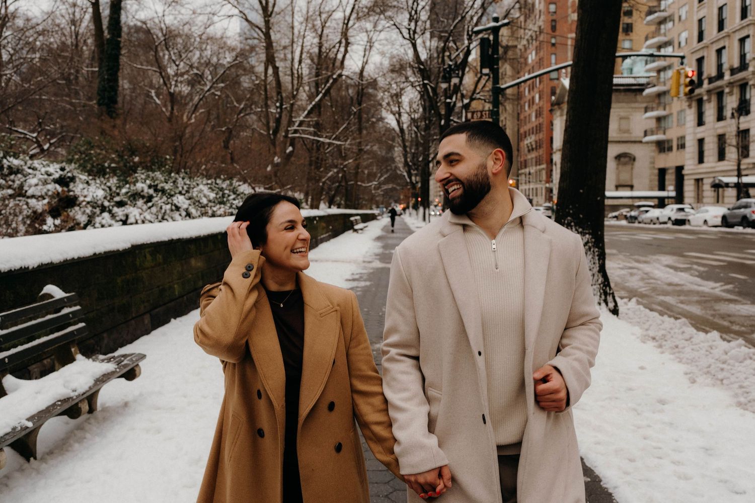 Joyful couple walking together in snowy urban central park setting.