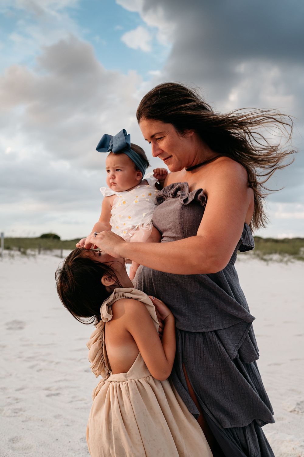 Family members share an intimate moment on a beach with dramatic cloudy skies in the background.