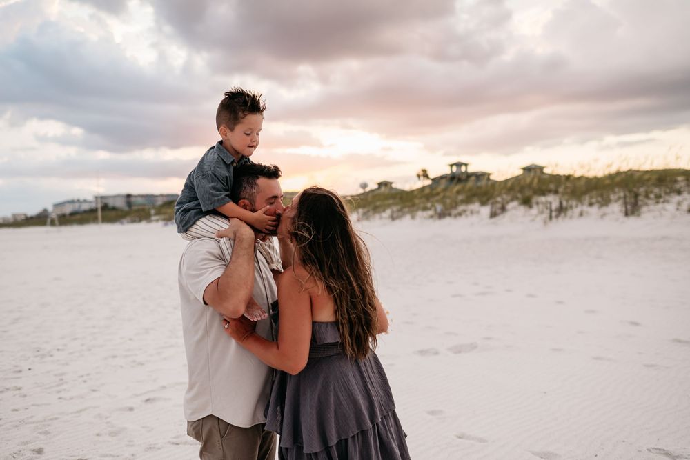 Loving family moment on a sandy beach at sunset with dramatic clouds overhead.