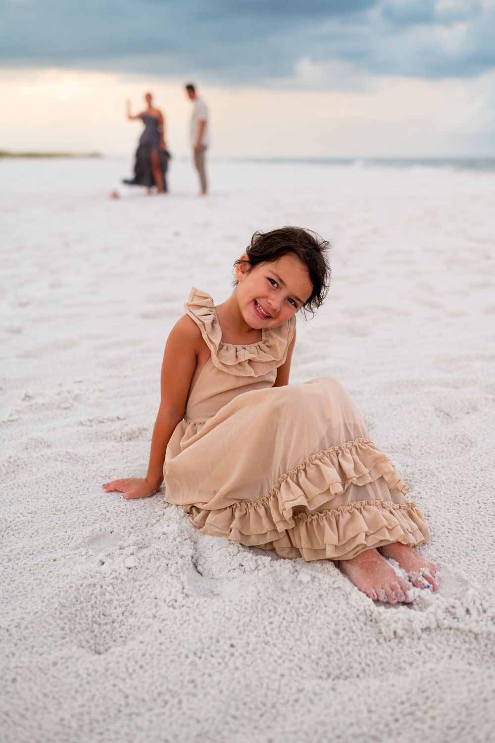 A person in a ruffled beige dress playfully poses on pristine white sand beach.