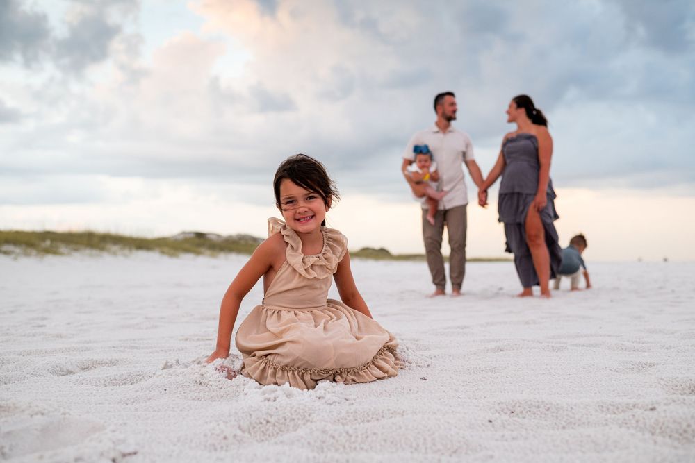 People playing and sitting in the soft white sand during a cloudy beach day.