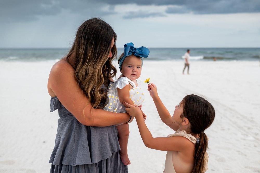 A joyful family moment captured on a pristine white sandy beach with stormy clouds overhead.