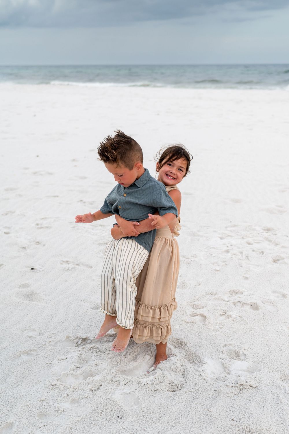 Two children playing and embracing on a white sandy beach by the ocean.
