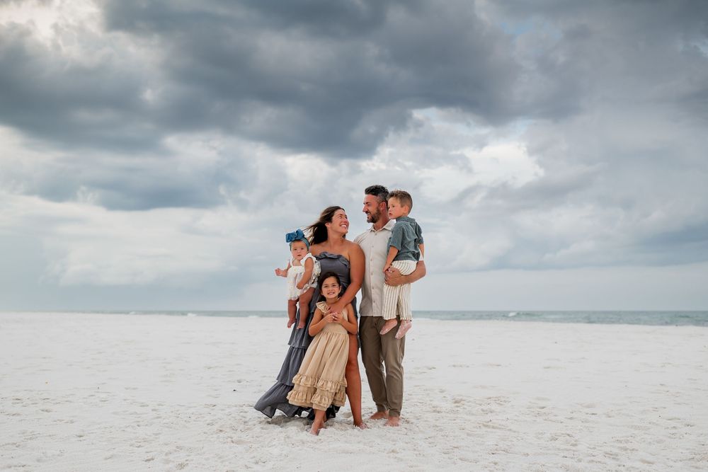 Family standing together on white sand beach under dramatic cloudy sky.
