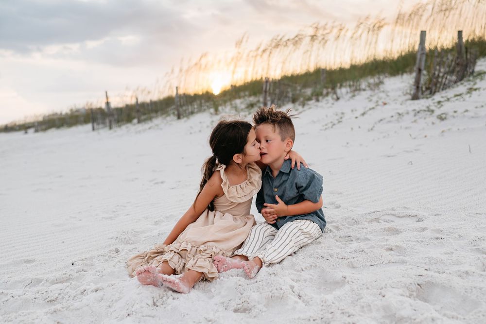 A couple embraces romantically on a white sandy beach during sunset.