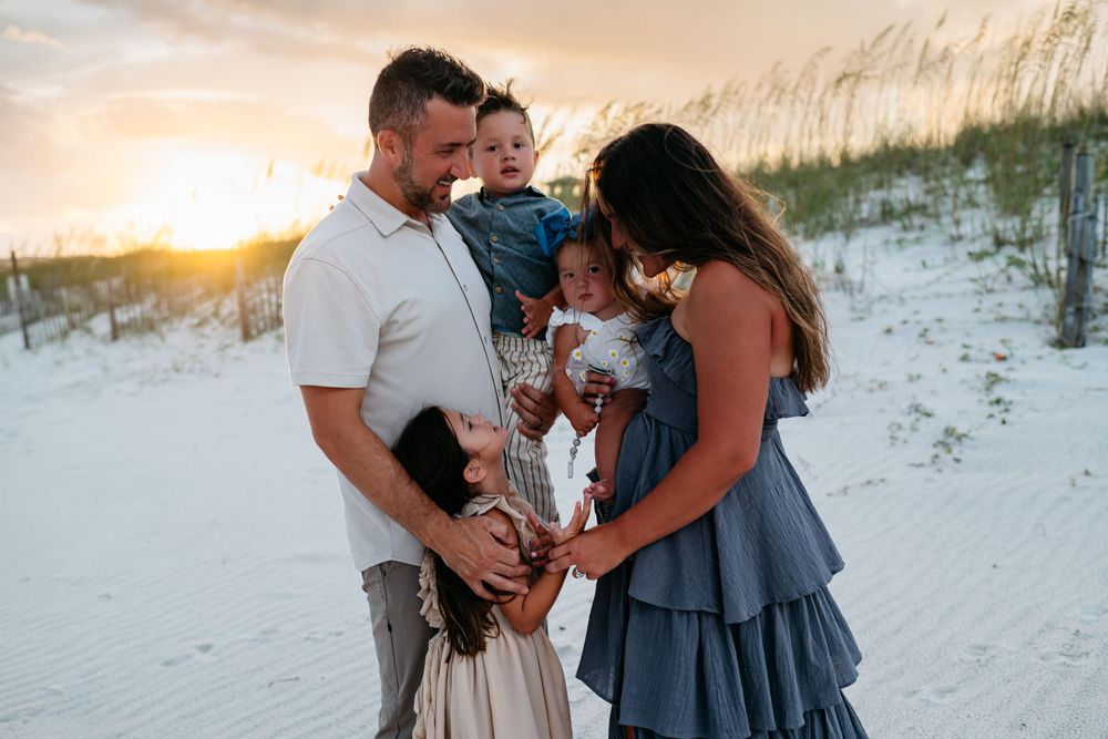A family shares tender moments together on a white sandy beach at sunset.