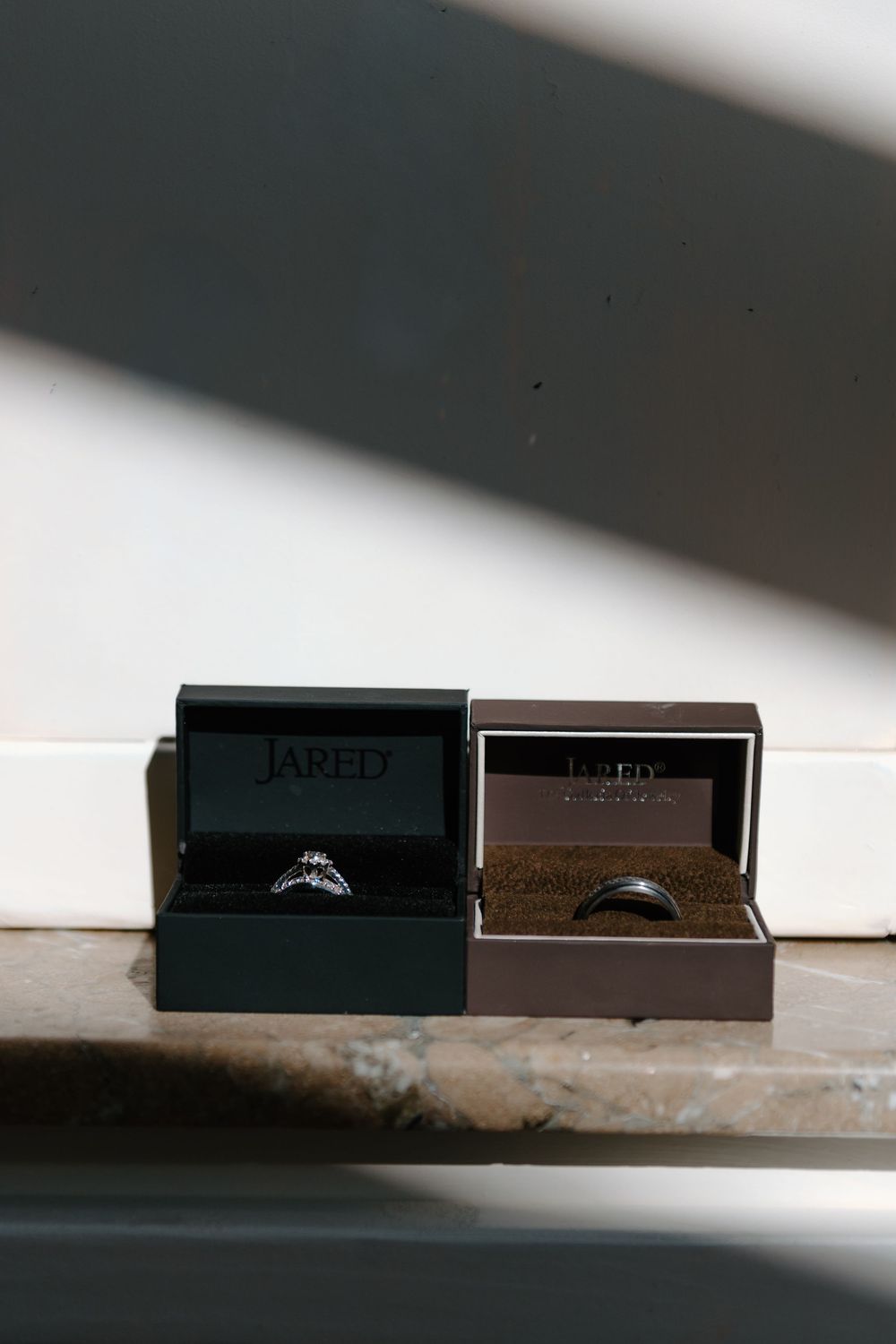 Two wedding rings displayed in black and brown jewelry boxes from Jared sitting on a white surface.