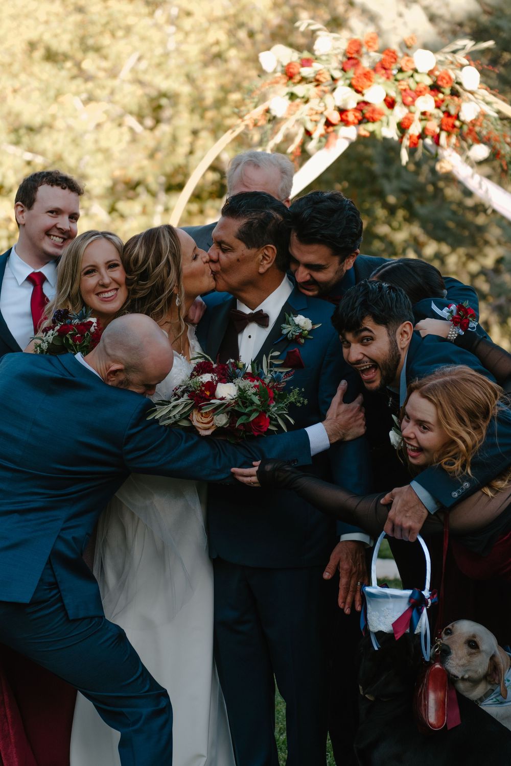 A wedding party hugs and laughs together in a candid group photo during golden hour.