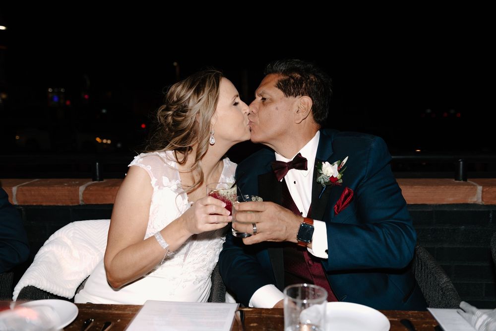 A couple shares a romantic kiss at a wedding reception while seated at a dining table.