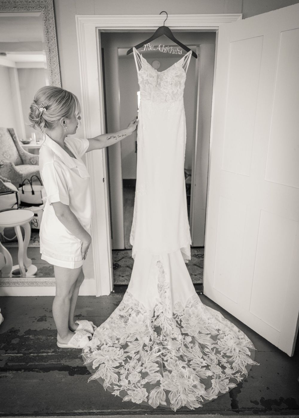 Elegant white lace wedding dress displayed on hangers in a preparation room.