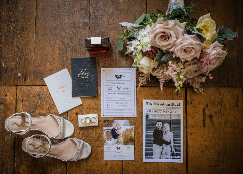 Wedding details including invitations, rings, shoes and flowers arranged on rustic wooden surface.