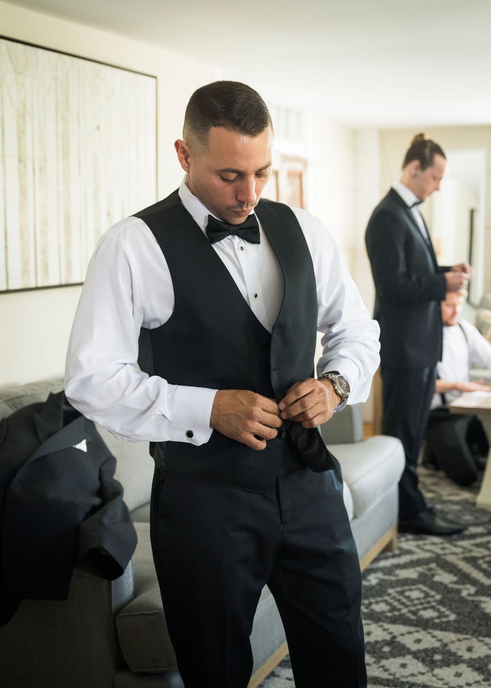 A person in formal attire adjusts their collar while getting ready in a hotel room.