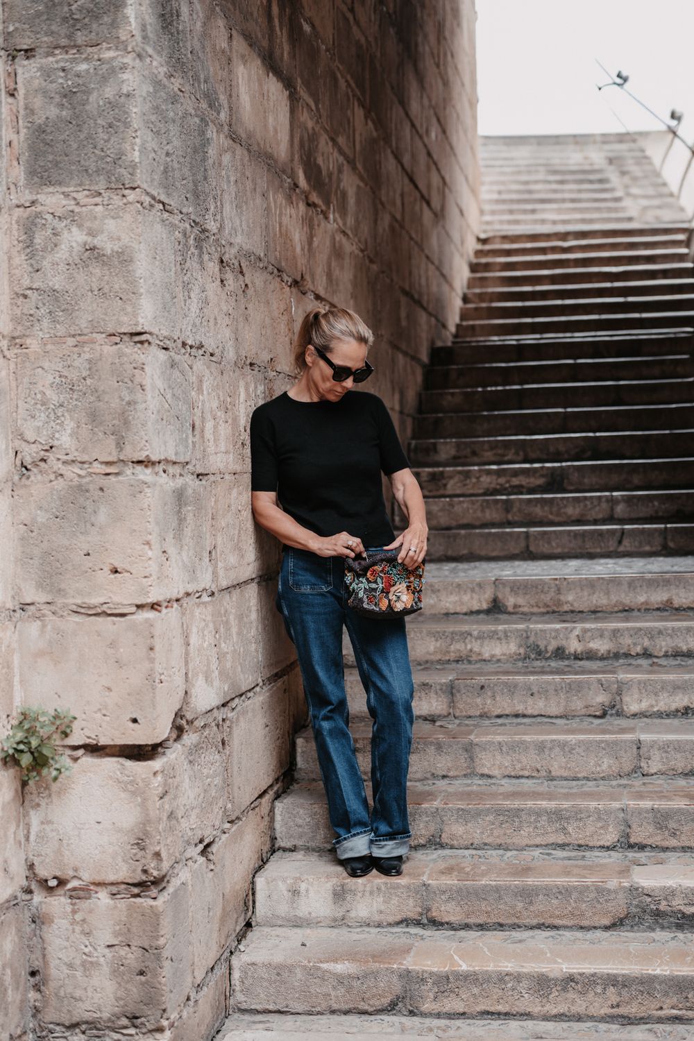 Farbfoto einer Frau auf den Treppen einer Kathedrale auf Mallorca, an den Aufgang gelehnt und in die Handtasche blickend.