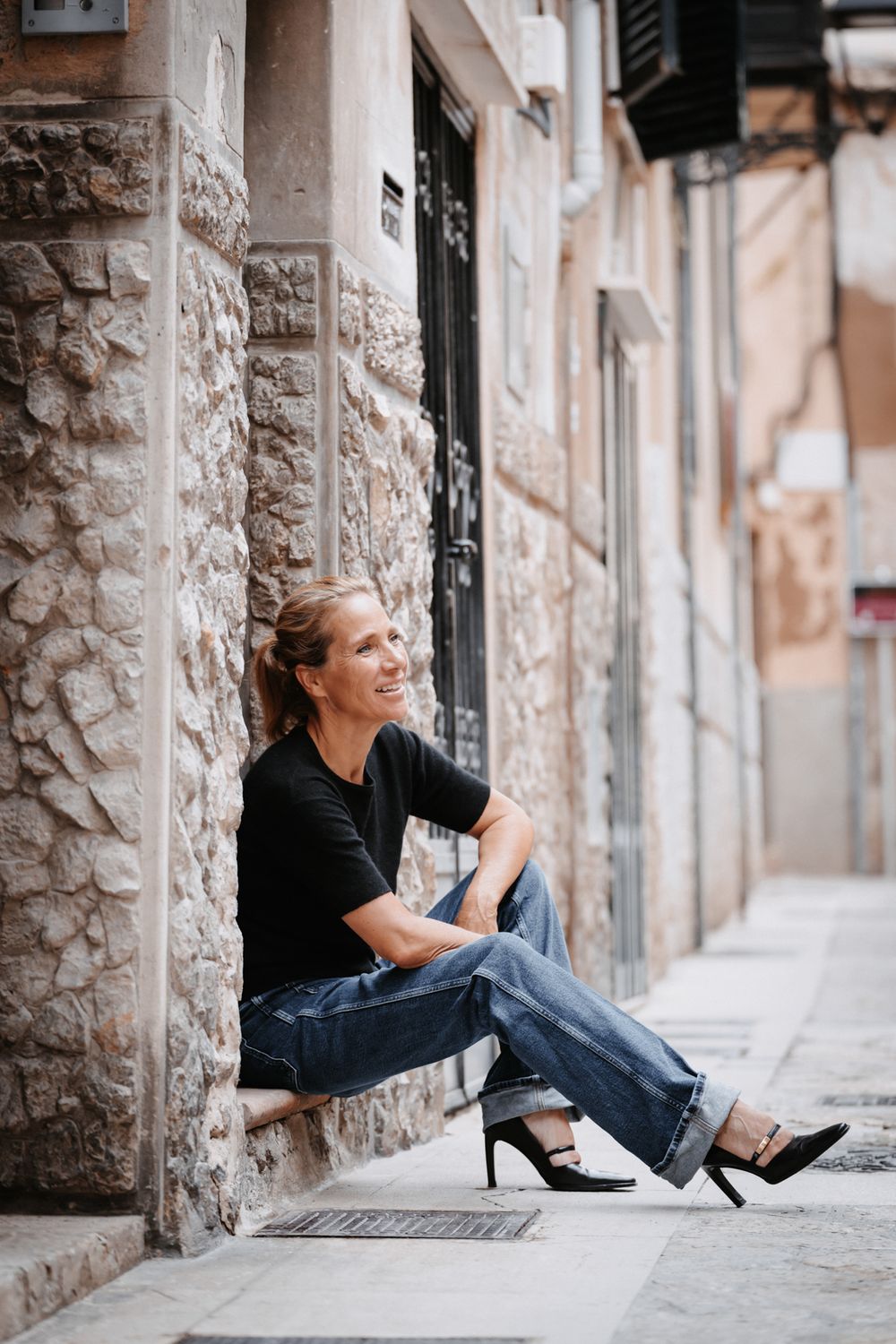 Farbfoto einer Frau in Jeans und High Heels auf einer Fensterbank in der Altstadt von Palma sitzend.
