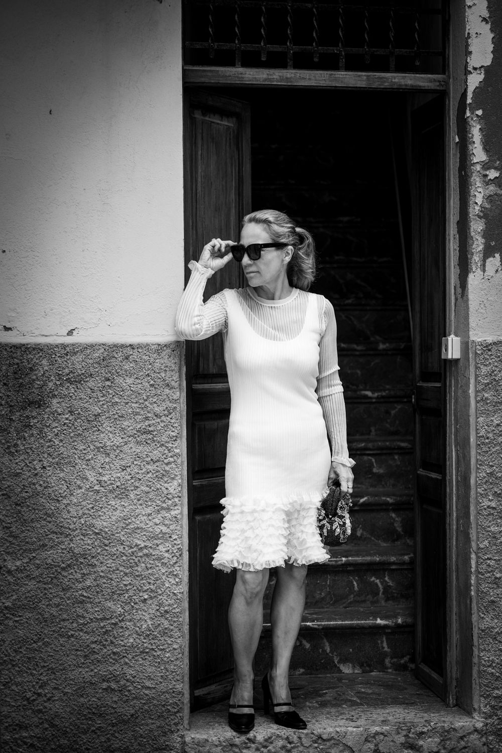 Schwarz-Weiß-Foto einer Frau im eleganten Kleid an einem Hauseingang in Palmas Altstadt, Treppen im Hintergrund.