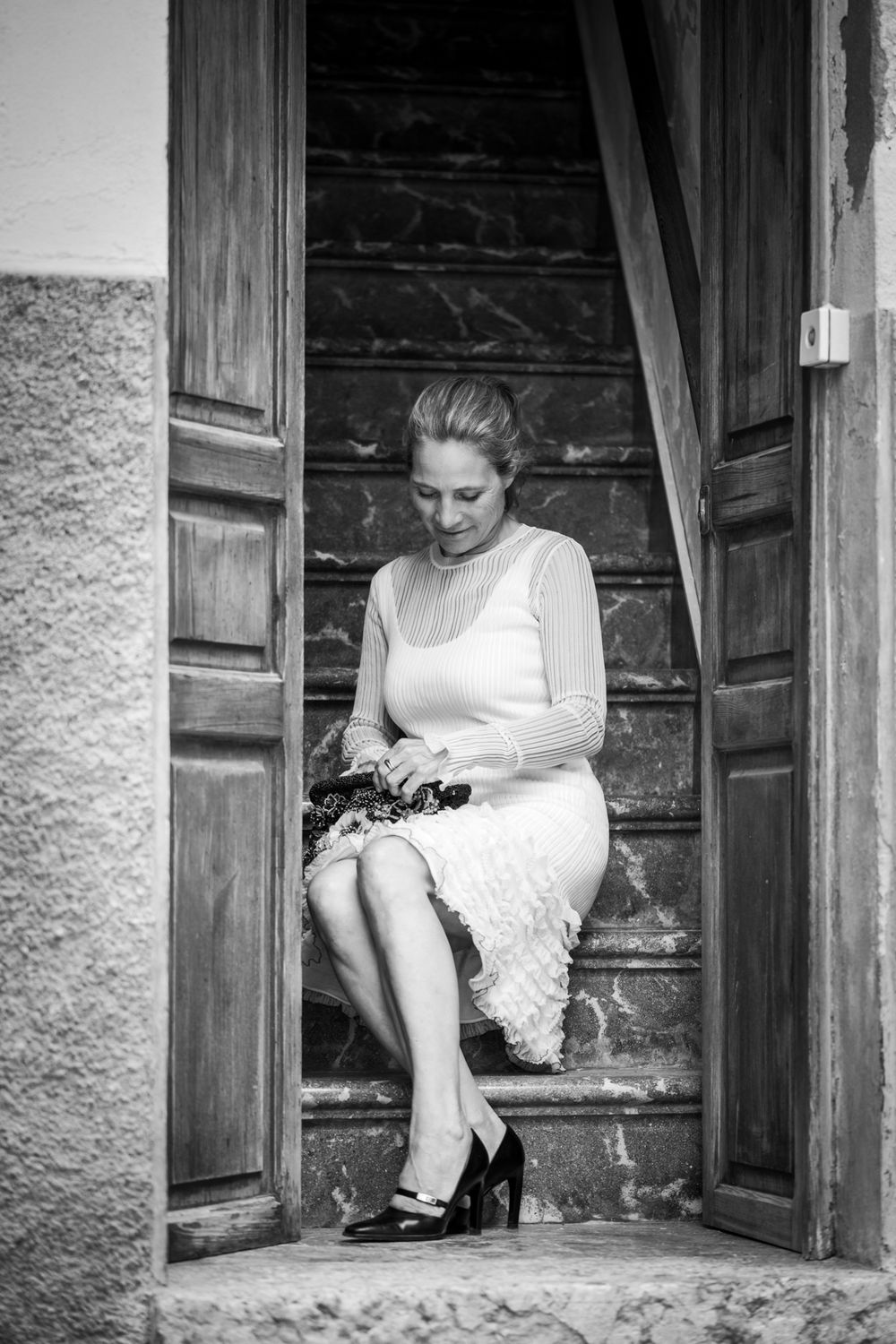 Schwarz-Weiß-Foto einer Frau auf alten Treppen in Palmas Altstadt, sitzend und in ihrer Handtasche suchend.