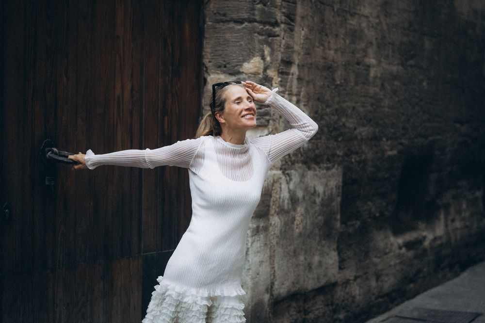 Farbfoto einer Frau in weißem Designerkleid an einer Tür in Palmas Altstadt, mit Blick in den Himmel