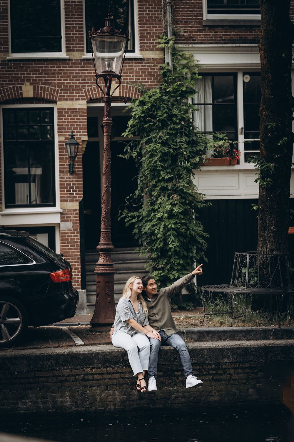 Paar sitzt an einer Gracht in Amsterdam und blickt gemeinsam in den Himmel – romantisches Pärchenshooting in urbaner Kulisse