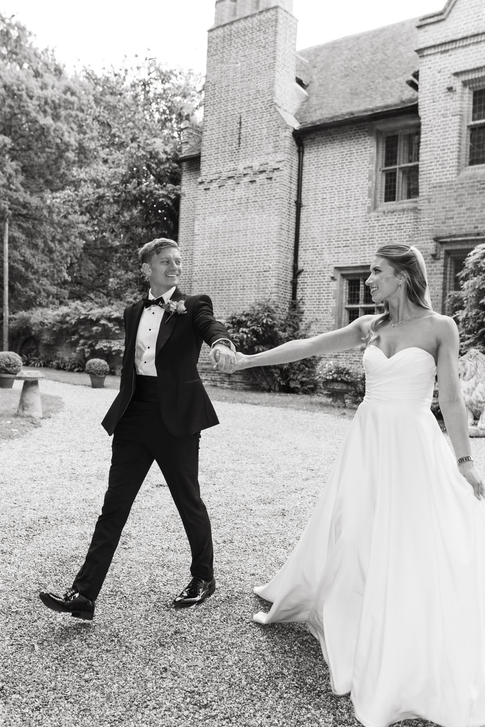Black and white photo series showing wedding couple playfully dancing and spinning together on a lawn outside a brick building.