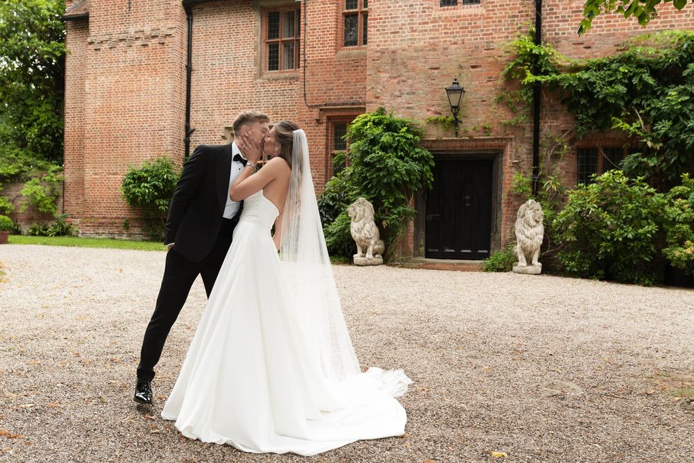 Elegant couple in formal wedding attire sharing an intimate moment in front of a rustic brick building.
